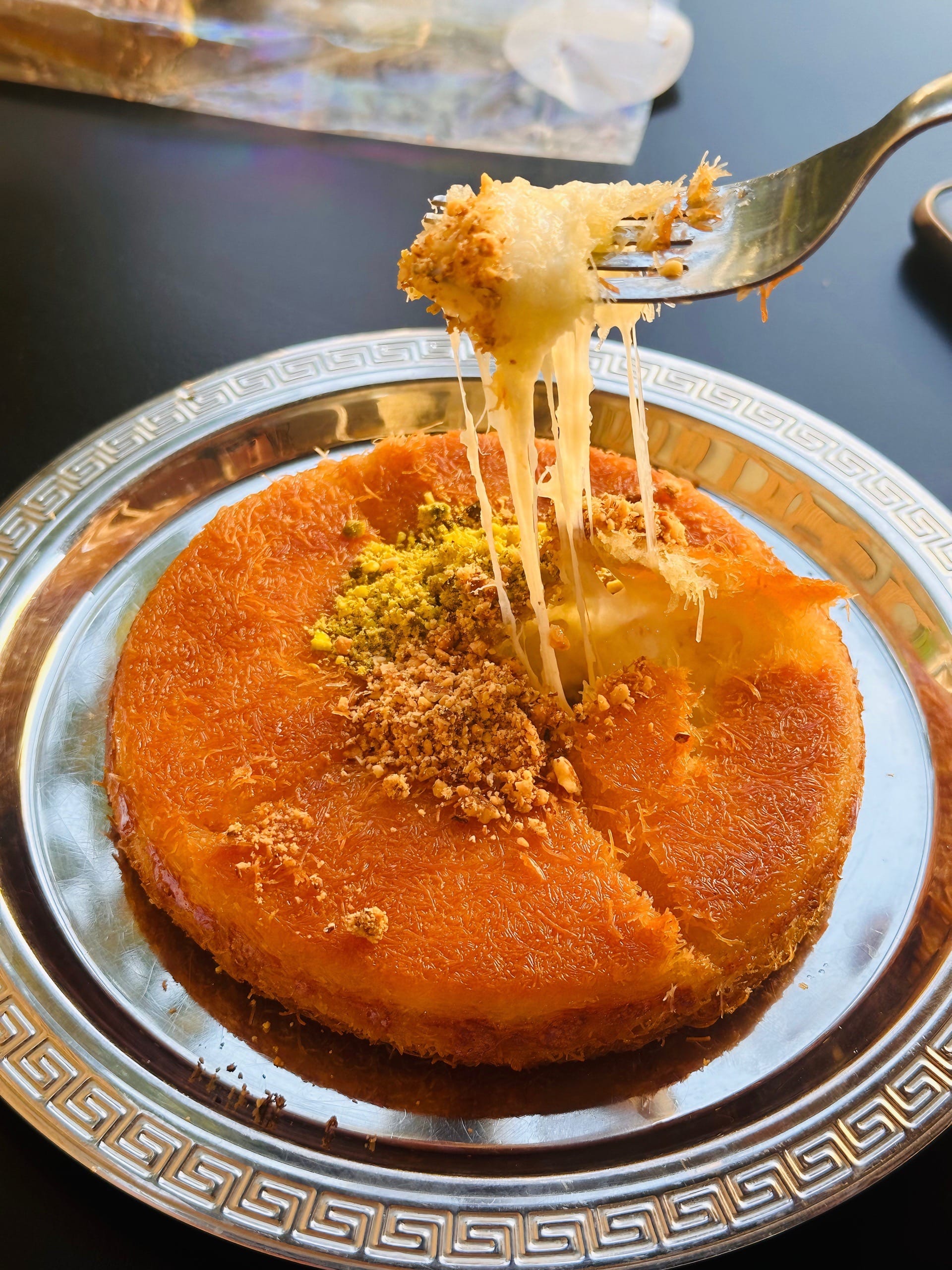 Un kunafa baklava doré et croustillant, garni de pistaches concassées, prêt à être dégusté.